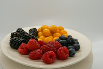 Brightly colored fresh berries on a white plate in front of a white background