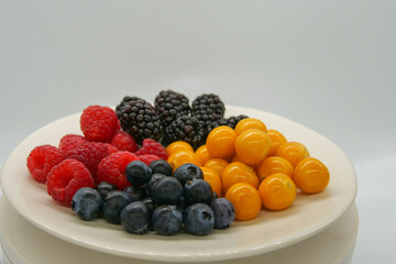 Brightly colored fresh berries on a white plate in front of a white background