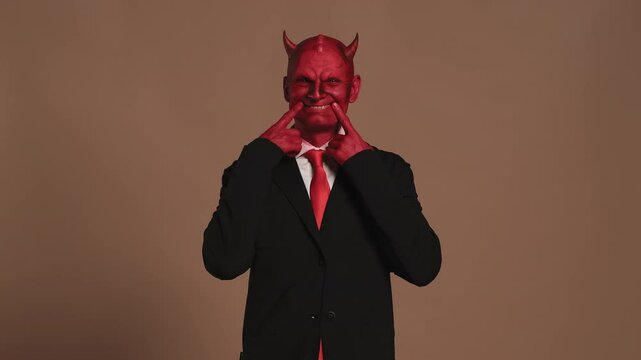 Red devil businessman forcing a smile on brown background