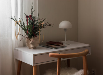 Cozy interior - a Christmas bouquet in a vase, a table lamp, a laptop, a notebook on a white table