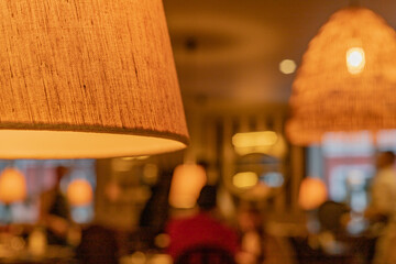 a close-up of a lampshade in a restaurant or cafe. Defocused images of people and the cafe interior background. Warm light.
