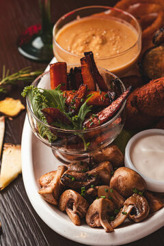Tabla de aperitivos vegetarianos con champi&ntilde;ones salteados, bastones de vegetales asados y salsas gourmet en un bar. Concepto de picoteo saludable y comida plant-based.