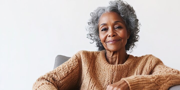 nostalgic 75-year-old african american woman wearing cozy knitted sweater sitting on chair with wistful smile gazing