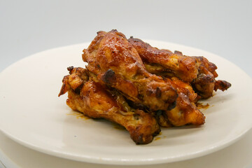 White plate with small brown basted and cooked chickenwings.