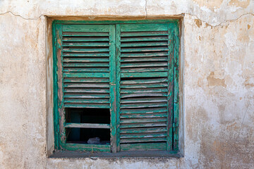 Fototapeta premium A rustic green wooden shutter on an old weathered wall in Lavrio, Greece, showcases the charm of decay with peeling paint and natural textures in the coastal town