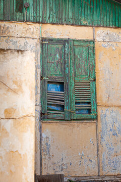 A rustic green wooden shutter on an old weathered wall in Lavrio, Greece, showcases the charm of decay with peeling paint and natural textures in the coastal town