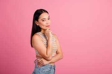 Stylish young woman with long brunette hair posing against a vibrant pink backdrop in a trendy summer outfit