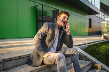 young handsome man sit on staircase and talk on mobile phone