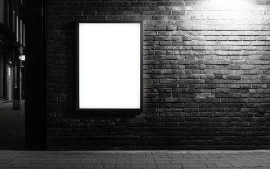 A blank white poster frame on an outdoor brick wall, softly illuminated by black lighting. 