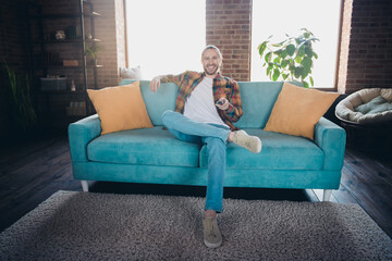 Young man in plaid shirt enjoying a relaxing day indoors on a cozy sofa, remote in hand, in a stylish loft apartment