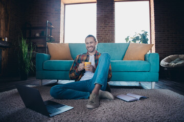 Obraz premium Young man enjoying a relaxed weekend at home with a cup of coffee, sitting on the floor in a stylish living room