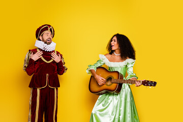 Fototapeta premium Young couple dressed in vintage costumes posing with a musical instrument against a vibrant yellow backdrop