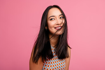 Joyful young woman with long brunette hair smiling against a vibrant pink background promoting...