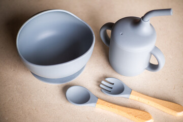 Silicone baby tableware set in gray, the first soft cup for toddlers. Baby eating utensils. Nutrition and feeding concept