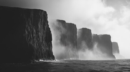 Dramatic black and white cliffs shrouded in mist with turbulent ocean waves beneath a cloudy sky atmosphere