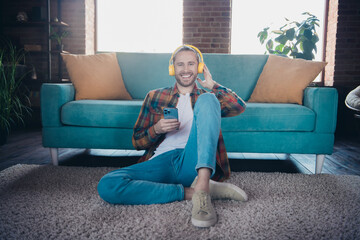 Cheerful young man enjoying music on headphones while sitting in a stylish loft living room