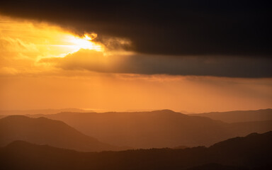 Bright sun rays shining through dark clouds over mountain at sunset. Dramatic sky in winter.