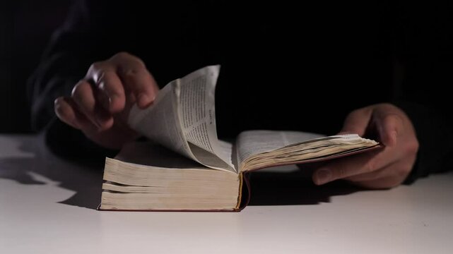 Hands turning page of old book Bible on white table in dark room