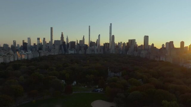 Aerial views showcase a sunset over Central Park, illuminating vibrant trees against the iconic Midtown Manhattan skyline. Warm evening light enhances the scene
