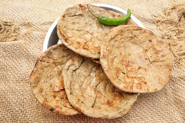 Traditional Indian bajre ki roti served with fresh green chili, showcasing rustic flavors and...