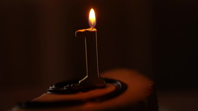 A cake with a minimum of details, decorated with one thin candle in the middle, the number 1. A hand brings a lighter to the candle and lights a fire. High quality 4k footage