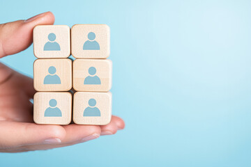 Hand holding wooden blocks with human icons, symbolizing teamwork and collaboration in a modern workplace.