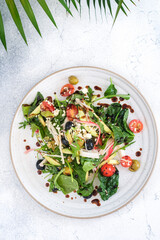 A fresh and colorful vegetable salad featuring spinach, cherry tomatoes, avocado, olives, and sesame seeds, served on a ceramic plate and topped with balsamic glaze.