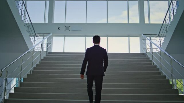 Elegant entrepreneur climbing stairs in modern office back view. Businessman - Powered by Adobe