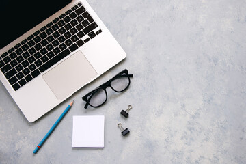 Gray desk office with laptop, glasses, pencil and blank paper.