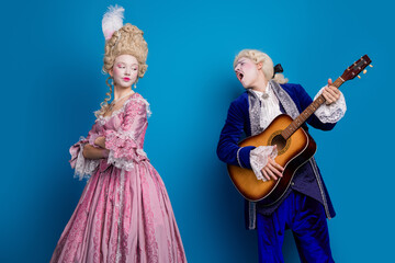 A charming historical couple dressed in elegant baroque costumes against a blue backdrop