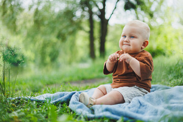 Little boy 1 year old sitting on the grass in the park and eating bread. Baby on a walk in the fresh air.