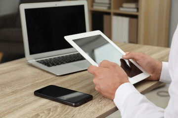 Businessman with tablet, smartphone and laptop at wooden table, closeup. Modern technology