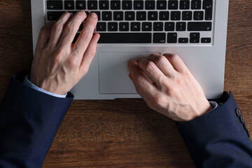 Businessman using laptop at wooden table, top view. Modern technology