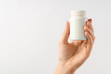 Woman holding medical bottle with pills on white background, closeup. Space for text