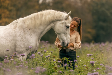A young woman cuddle and interact with her white spanish horese on a wildflower field in autumn...