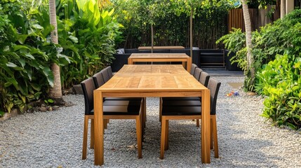 Obraz premium Wooden dining table with black chairs in a serene garden setting surrounded by lush greenery and gravel pathway