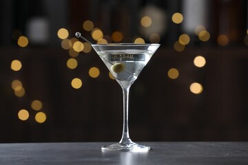 Martini cocktail with olive in glass on grey table against blurred background. Bokeh effect