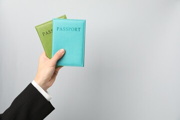 Woman holding passports in bright covers on grey background, closeup. Space for text