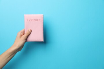 Woman holding passport in bright cover on light blue background, closeup. Space for text