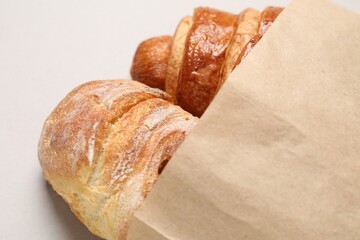 Paper bag with fresh baguette and croissant on light gray table, closeup