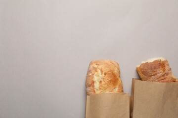 Paper bags with fresh baguettes on gray table, top view. Space for text
