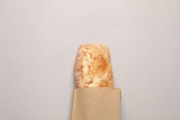 Paper bag with fresh baguette on light gray table, top view. Space for text