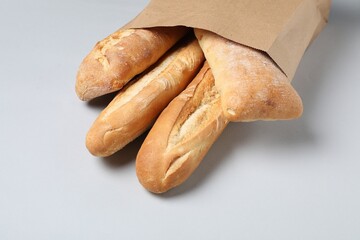 Paper bag with fresh baguettes and ciabatta on white background, closeup