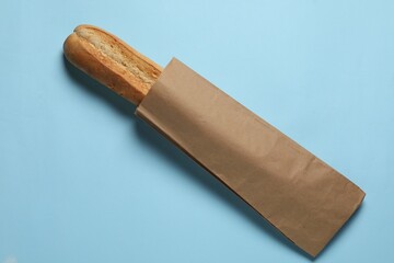 Paper bag with fresh baguette on light blue background, top view