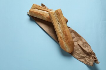 Paper bag and fresh baguette on light blue background, top view. Space for text