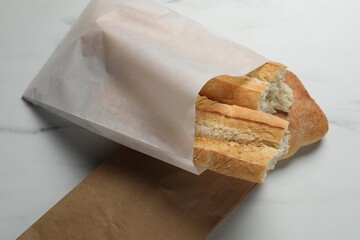 Paper bags with fresh baguette and ciabatta on white marble table, above view