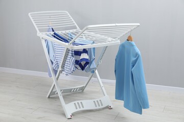Drying rack with fresh clean laundry near grey wall