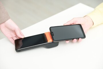 Woman paying for service with smartphone via terminal at white table indoors, closeup