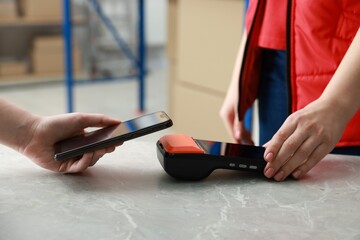 Woman paying for service with smartphone via terminal at table indoors, closeup