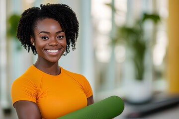Fototapeta premium Fit and confident African yoga instructor in orange sportswear, gripping a mat in a spacious studio. Copy space.